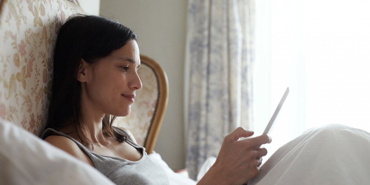 Woman lying down in bed with tablet