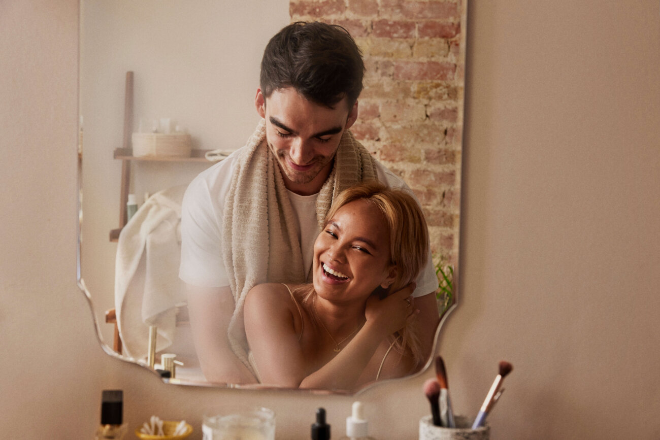 Brown haired man and blond woman standing in front of a mirror